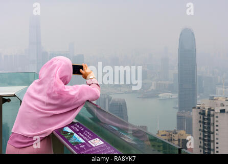 Woman takes a mobile phone photo on the deck of The Peak Tower viewing platform restricted by the haze from air pollution, Hong Kong Stock Photo