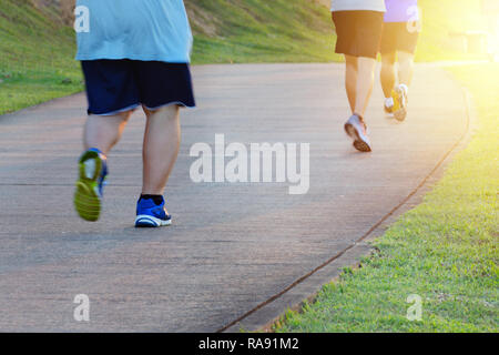 Fat man jogging, catching up with thin men. Low angle view of runners running in park. Blurred feet motion group of runners, Fitness and healthy Stock Photo