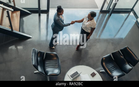 Two friendly african business woman shaking hands in office environment Stock Photo