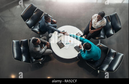 Group of African business people sitting and discussing statistics during a sit down meeting taking from above. Two colleagues are shaking hands Stock Photo