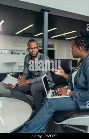 Two african business people talking seriously with hand gestures during a meeting using their laptop and tablet Stock Photo
