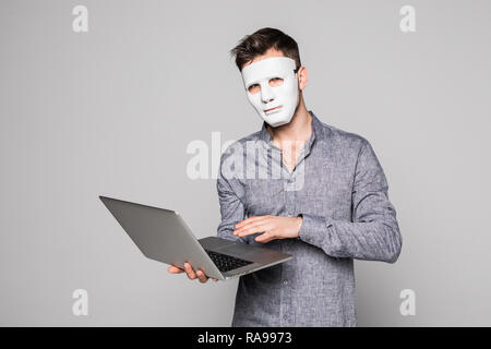 Hacker with anonymous mask with laptop while standing against white background Stock Photo