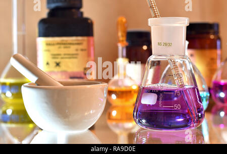 Laboratory glassware with colorful solutions and chemicals in the background Stock Photo