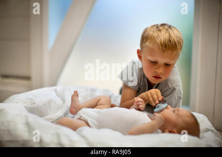 Young Boy looking over baby boy holding his dummy in. Stock Photo