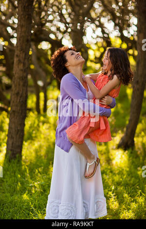 Laughing mid adult woman holding her daughter as they stand together in a forest. Stock Photo