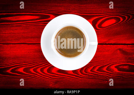 Overhead view of a freshly brewed mug of espresso coffee on red rustic wooden background with woodgrain texture. Coffee break style, concept Stock Photo