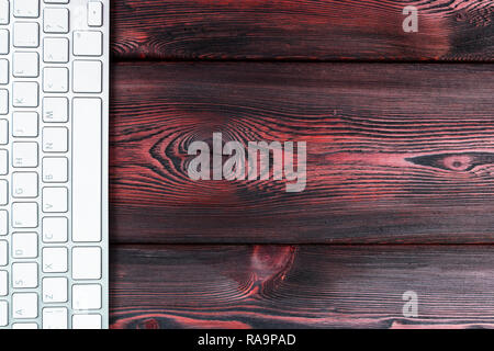 Close up view of a business workplace with wireless computer keyboard, keys on old red dark natural wooden table background. Office desk with copy spa Stock Photo