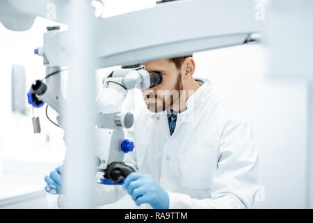 Male dentist examining patient looking on the teeth with professional microscope at surgery dental office Stock Photo