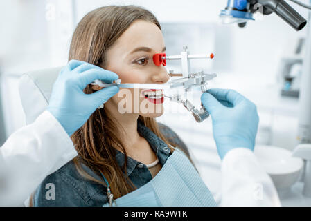 Dentist putting jaw measurement system to a young woman patient in the dental office Stock Photo