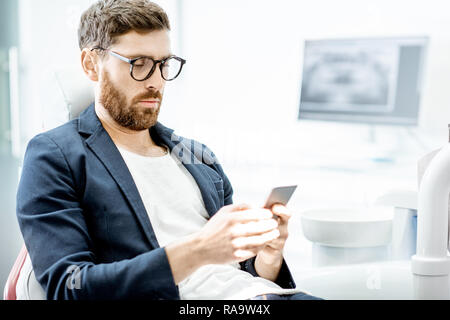 Portrait of a handsome businessman with phone sitting on the dental chair in the dental office Stock Photo
