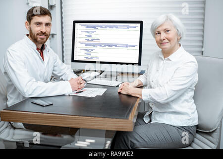 Portrait of a senior woman and handsome doctor sitting during the consultation in the office Stock Photo