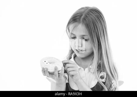 Sweet treasure. Girl calm face carefully holds sweet donut in hand, isolated white. Kid girl with long hair likes donuts. Snack concept. Child likes to eat donuts with colorful toppings, copy space. Stock Photo