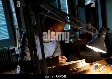female craftsman violin maker working on a new violin in the workshop Stock Photo