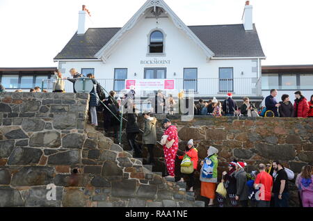 Traditional Boxing Day swimmers climb steps to promenade at The Rockmount Hotel, Cobo Bay, Guernsey, Channel Islands, UK. Stock Photo