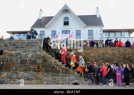 Traditional Boxing Day swimmers climb steps to promenade at The Rockmount Hotel, Cobo Bay, Guernsey, Channel Islands, UK. Stock Photo