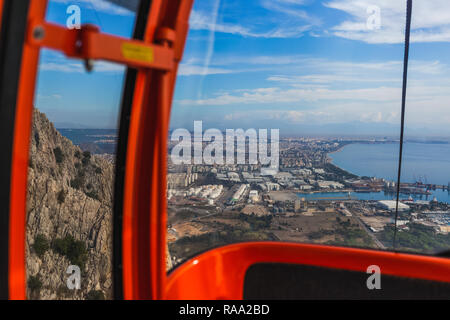Inside of red cabin of cableway on picturesque mountains. Cabin driving over huge mountains. Beautiful view at city in distance. Horizontal color phot Stock Photo