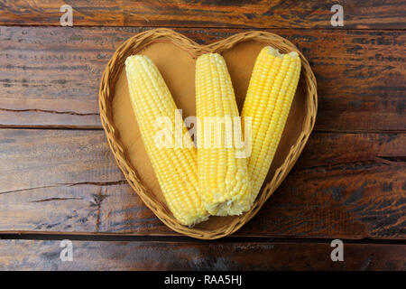 Corn cob, fresh, harvested from plantation inside basket with heart shape on rustic wooden table. space for text Stock Photo