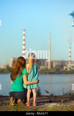 care future concept. Young mother with her kids are looking at the chimney-stalks polluting an air Stock Photo
