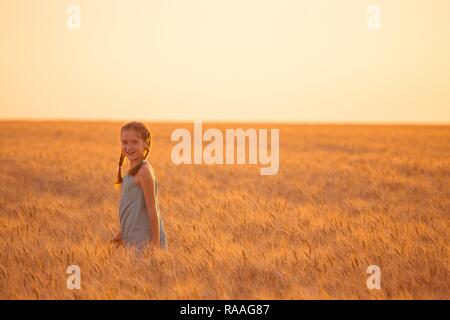 young girl joys on the wheat field at the sunset time Stock Photo