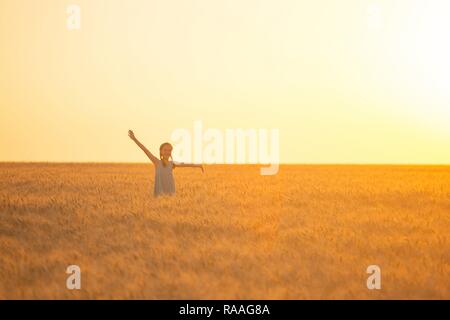 young girl joys on the wheat field at the sunset time Stock Photo