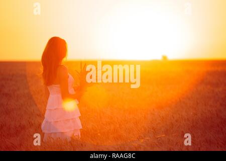 young girl joys on the wheat field at the sunset time Stock Photo