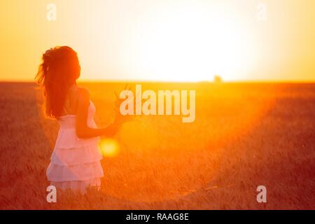 young girl joys on the wheat field at the sunset time Stock Photo