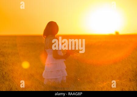 young girl joys on the wheat field at the sunset time Stock Photo