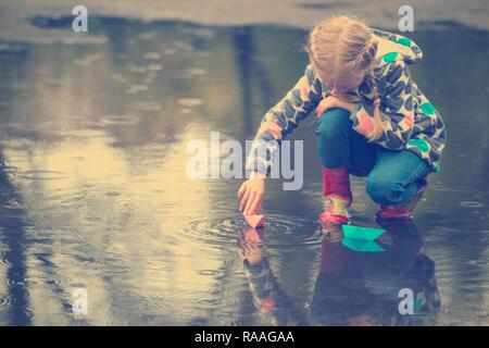 girl runs the pink paper boat in a puddle in the rain, spring Stock Photo