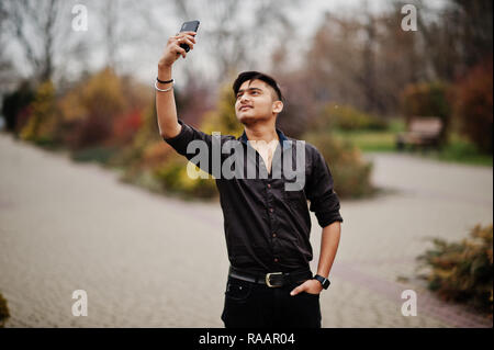 Indian man in brown shirt posed outdoor and making selfie on mobile phone. Stock Photo