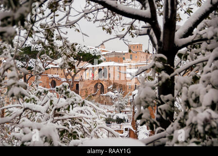 Frozen Rome. View of Trajan's Forum and Imperial Fora Avenue ancient ruins covered by snow through tree branches Stock Photo