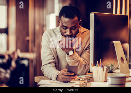 Serious dark-skinned man staring at his smartphone Stock Photo