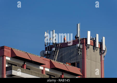 Cellphone antennas and a telecommunications workers on top of an apartment building in Vancouver, BC, Canada Stock Photo
