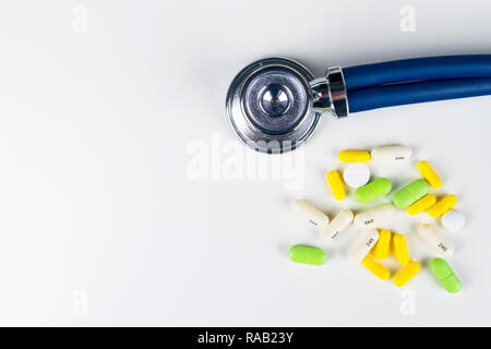 Medical stethoscope lying on white table with pile of pills. Cardiology care health protection prevention and help. Healthy life or insurance concept. Stock Photo