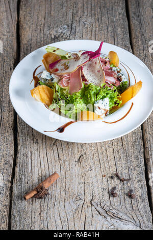 Salad with slices of bacon, persimmon and pieces of gorgonzola is beautifully presented on a white plate. Stock Photo