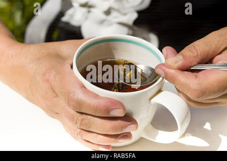 A woman taking wasp out of tea cup, outdoor close-up Stock Photo