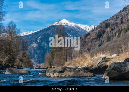 The Noce River surrounded by hills with snow-capped mountains - italian alps. In the distance Pellizzano city, Trento, Trentino, Italy Stock Photo