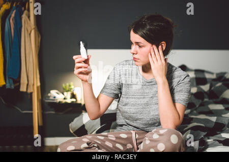 The theme is seasonal cold, runny nose flu virus infection. Young caucasian woman at home bedroom bed uses spray drops of medicine in her nose for sno Stock Photo