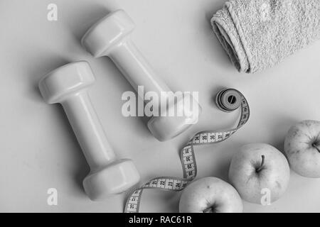 Sports and healthy regime equipment, top view. Dumbbells in bright green color, measure tape, towel and fruit on green background. Athletics and weight loss concept. Barbells near juicy green apple Stock Photo