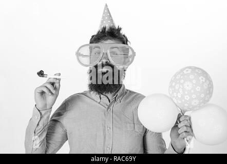 Party concept. Hipster in giant sunglasses celebrating birthday. Guy in party hat with party horn celebrates. Man with beard and mustache on happy face holds air balloons, white background. Stock Photo