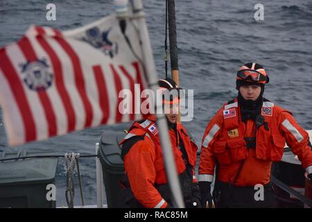 Petty Officer 1st Class Andrew Yeckley and Petty Officer 2nd Class Andrew Ayriss of the Coast Guard Cutter Anacapa, wait to conduct a boarding in the Icy Straits of Alaska, while the Coast Guard Ensign waves overhead, Jan. 14, 2017.    The Coast Guard Cutter Anacapa is a 110-ft patrol boat homeported in Petersburg, Alaska.    Coast Guard Stock Photo