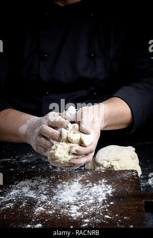 baker kneads white wheat flour dough on a brown  wooden table Stock Photo
