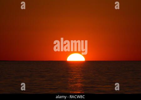 Half red hot African sun setting behind the horizon and a rippled Lake Kariba, Zimbabwe Stock Photo