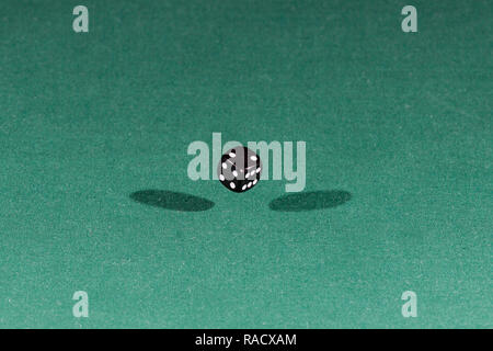 One black dice falling on a green table Stock Photo