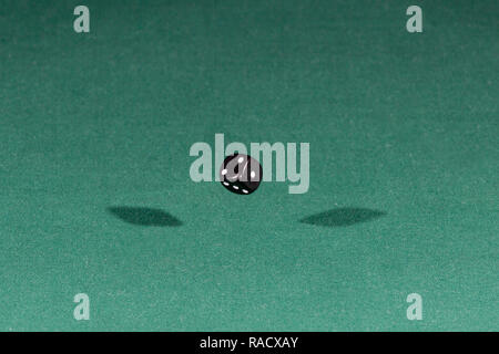 One black dice falling on a green table Stock Photo
