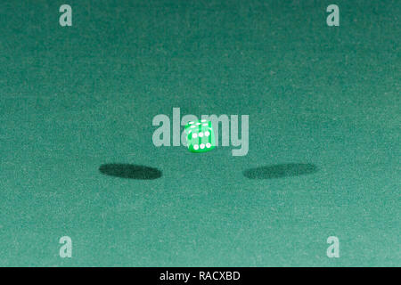 One green dice falling on a green table Stock Photo