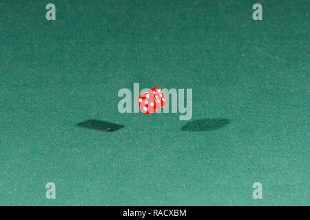 One red dice falling on a green table Stock Photo