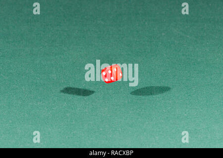 One red dice falling on a green table Stock Photo