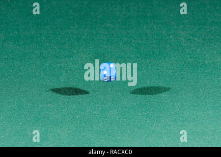 One blue dice falling on a green table Stock Photo