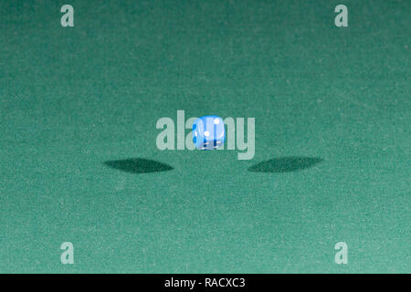 One blue dice falling on a green table Stock Photo