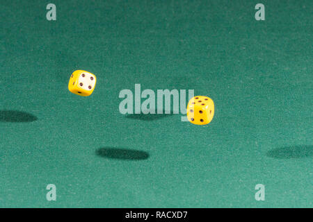 Two yellow dices falling on a green table Stock Photo